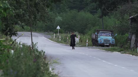 Old-Georgian-Woman-in-traditional-black-attire-crossing-the-road-in-the-Georgian-Rural-countryside---Wide-static-shot