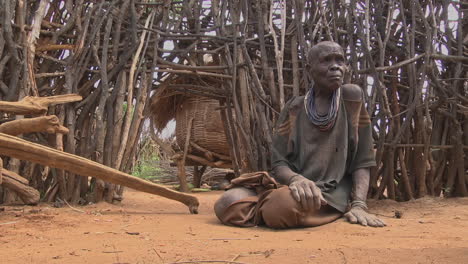 Old-Rwandan-Tribes-Woman-Sitting-On-Dirt-Floor-With-Sticks-In-The-Background