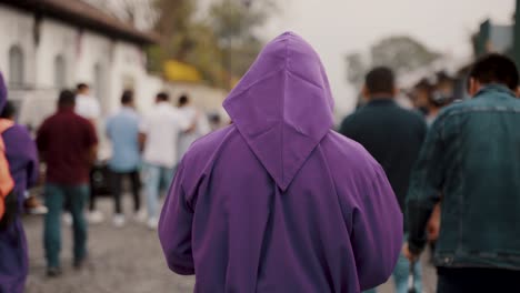 Cucurucho-In-Purple-Tunica-Walking-With-Catholic-Devotees-On-The-Street-During-Semana-Santa-Procession-In-Antigua,-Guatemala