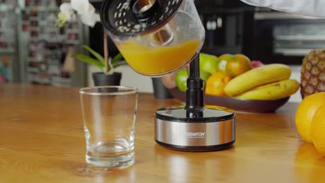 Woman-pouring-freshly-squeezed-orange-juice-into-glass-from-electric-juicer