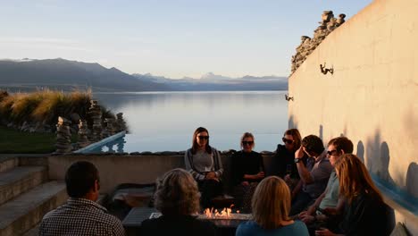 Group-of-friends-sitting-around-fireplace-drinking-beer-with-spectacular-view-of-Mount-Cook-and-Lake-Pukaki