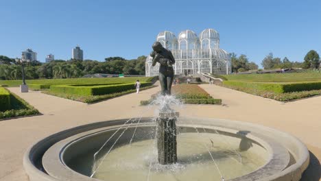 Botanical-Garden-of-Curitiba,-gardens-with-the-statue-"Amor-Maternal"-and-the-greenhouse-"Palácio-de-Cristal"-in-art-nouveau-style