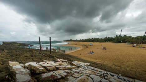 Ominous-rain-clouds-roll-over-La-Poza-del-Obispo-Beach-and-summer-tourists,-Arecibo,-Puerto-Rico,-USA---Timelapse
