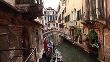 Gondolier-waiting-in-his-gondola-in-a-small-Venetian-canal-in-Venice,-Italy