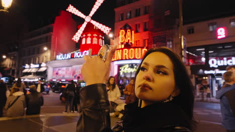 Mujer-Modelo-Aplicando-Maquillaje-Frente-Al-Espejo-Por-La-Noche-En-La-Calle-Frente-Al-Moulin-Rouge,-Ciudad-De-París