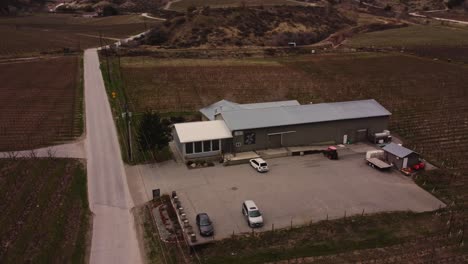 small-tin-roof-of-intersection-winery-in-okanagan-valley-amongst-vineyards-mountains-in-osoyoos-bc-canada-wide-orbiting-aerial-4k-stabilized