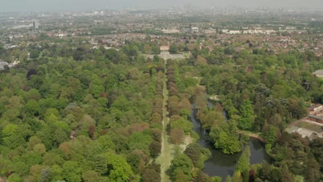 Aerial-shot-towards-Kew-Gardens-Palm-house-greenhouse-with-the-London-skyline-in-the-background