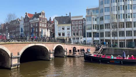 Canal-cruise-boat-with-tourists-goes-under-bridge-in-Amsterdam,-static-shot