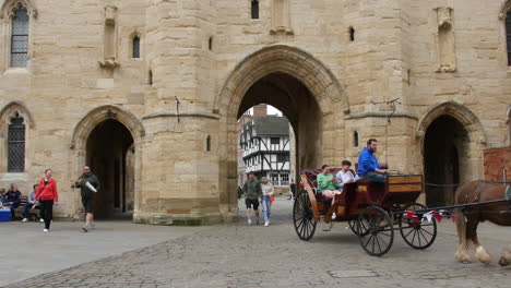 A-horse-drawn-carriage-travelling-through-an-archway-in-the-medieval-town-of-Lincoln-in-England