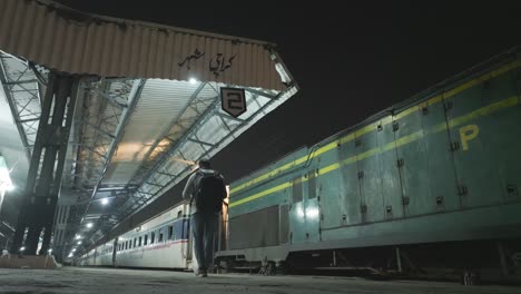 Hombre-Con-Mochila-Caminando-Por-La-Plataforma-Vacía-De-La-Estación-De-Tren-De-La-Ciudad-De-Karachi-Por-La-Noche