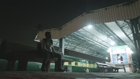 Low-angle-shot-of-man-sitting-on-a-bench-on-Karachi-City-railway-station-platform-in-Karachi,-Pakistan-at-night-time