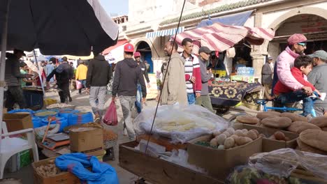 Tourists-and-local-people-passing-by-Street-market-stalls,-Essaouira-Medina,-Morocco