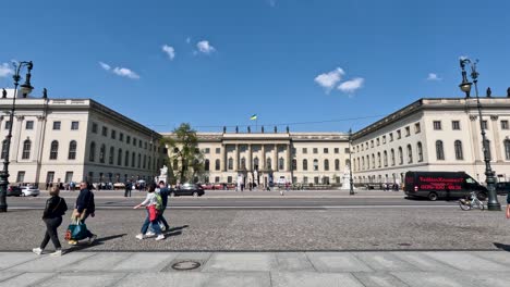 Traffic-And-People-Going-Past-View-Of-Humboldt-University-of-Berlin-On-Sunny-Day-With-Blue-Skies