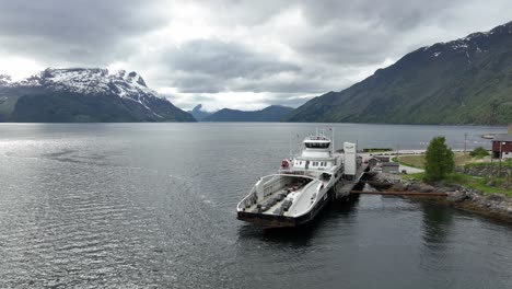 Electric-zero-emission-ferry-Eidsfjord-is-charging-batteries-from-ferry-charger-while-alongside-in-Lote-ferry-pier-in-western-Norway---Aerial-approaching-ferry-with-stunning-fjord-background