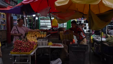 View-of-fruits-vendors-selling-fresh-fruits-and-a-customer-offering-a-stick-of-cigarette-in-Petaling-Street,-Kuala-Lumpur,-Malaysia