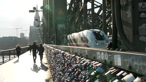 Love-Pad-Locks-On-Hohenzollern-Bridge-Fence-To-Symbolize-Love-And-Relationships-With-DB-ICE-Train-In-View-As-People-Walk-Past-With-Sun-Light-Lens-Flares