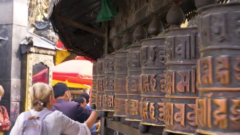 Nahaufnahme-Weiblicher-Touristenhände,-Die-über-Eine-Reihe-Von-Gebetsmühlen-Im-Tempel-In-Kathmandu,-Nepal,-Scrollen