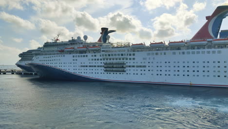 A-luxury-cruise-ship-Carnival,-Paradise-moving-backwards-on-port-and-revealing-another-cruise-ship-docked-on-port-video-background-in-4K-|-Carnival-cruise-ship-gracefully-sailing-away-from-the-port