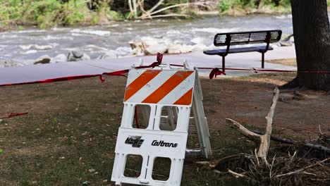 Caltrans-warning-caution-signage-in-front-of-the-raging-kern-river-in-Kernville-California-stopping-pedestrian-traffic-with-debris-laying-around