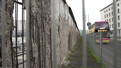 Looking-Along-Section-Of-Original-Berlin-Wall-At-Topography-of-Terror-In-Berlin-Through-Wire-Fence-And-Tourist-Bus-Approaching