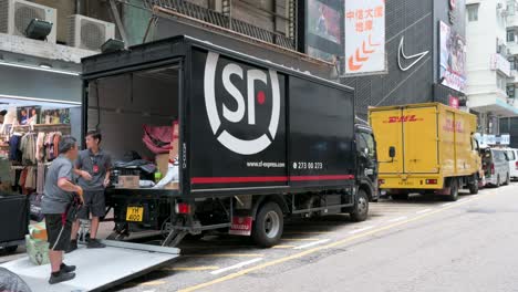 Workers-of-the-Chinese-delivery-company-SF-Express-manage-numerous-order-packages-at-its-delivery-truck-as-the-German-express-delivery-mail-company-DHL-truck-parked-in-the-street