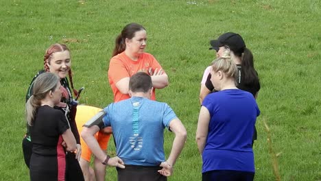 Group-club-of-runners-gathered-talking-and-supporting-each-other-in-local-park-field-at-start-of-their-fitness-run