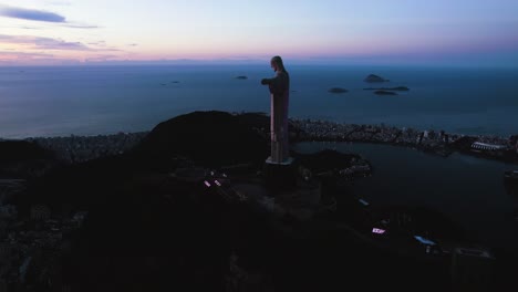 Aerial-view-circling-the-illuminated-Christ-the-Redeemer-statue,-in-Rio-de-Janeiro,-dusk-in-Brazil