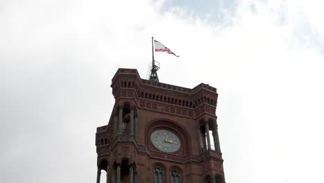 Looking-Up-At-Rotes-Rathaus-Clock-Tower-With-Flag-Of-Berlin-Fluttering-In-Wind-On-Flag-Pole
