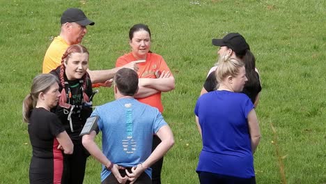 Group-of-runners-gathered-having-conversation-and-supporting-each-other-in-local-park-field-at-start-of-their-fitness-run