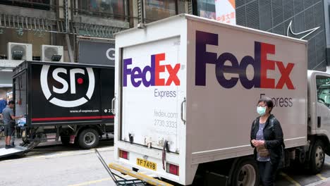 A-Chinese-delivery-company-SF-Express-delivery-truck-are-stationed-in-the-street-as-pedestrians-walk-through-the-frame