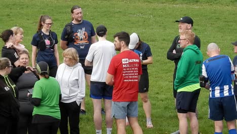 Group-of-runners-gathered-having-conversation-and-supporting-each-other-in-local-park-field-at-start-of-their-fitness-run