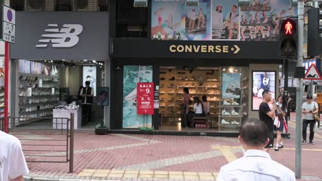 Pedestrians-and-shoppers-cross-the-street-in-front-of-the-American-footwear-brands-New-Balance-and-Converse-stores-and-logos