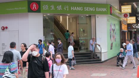 Fußgänger-Gehen-An-Dem-In-Hongkong-Ansässigen-Bank--Und-Finanzdienstleistungsunternehmen-Und-Dem-Hauptindikator-Für-Den-Hongkonger-Aktienmarkt,-Der-Hang-Seng-Bank-Und-Einer-Filiale-In-Hongkong-Vorbei