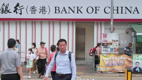 Chinese-pedestrians-walk-through-a-zebra-crossing-in-front-of-the-Chinese-state-owned-commercial-banking-company,-Bank-of-China,-branch