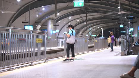 Thai-Woman-Waiting-for-The-Metro-On-Bangkok-BTS-Platform-at-Night-With-Few-People-Around,-Thailand