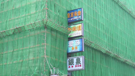 A-building-is-seen-under-maintenance-as-its-facade-is-covered-with-bamboo-scaffolding-and-a-green-net-while-commerce-street-signs-are-visible-to-the-public