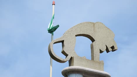 Rotterdam-Zoo-Stone-Carving-With-Flag-of-Rotterdam-Fluttering-In-Wind-Against-Clear-Blue-Sky-In-Background