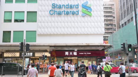 Fußgänger-Gehen-über-Die-Straße-Vor-Der-Standard-Chartered-Filiale-Des-Britischen-Multinationalen-Bank--Und-Finanzdienstleistungsunternehmens-In-Hongkong
