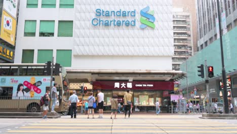 Pedestrians-walk-across-the-frame-as-the-British-multinational-banking-and-financial-services-company-Standard-Chartered-branch-is-seen-in-the-background