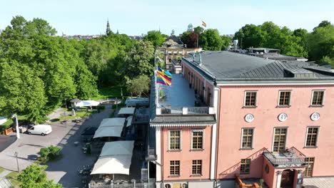 Pride-Rainbow-flag-waving-in-the-sun-together-with-scandinavian-flags-on-top-of-Nordic-hotel-in-Sweden---Hotel-Hasselbacken-Stockholm