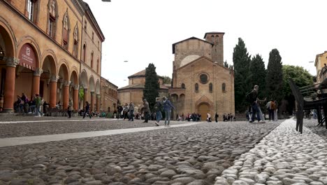 Tourists-Walking-Across-Piazza-Santo-Stefano-With-Basilica-of-Santo-Stefano-In-The-Background-In-Bologna