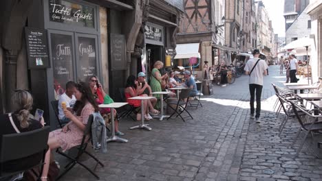A-young-man-walking-cobbled-street-of-Vieux-Tours-while-people-sitting-on-the-street-on-numerous-small-terraces