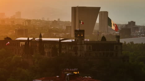 Telephoto-drone-shot-of-flags-on-the-sunlit-Castillo-de-Chapultepec,-in-Mexico