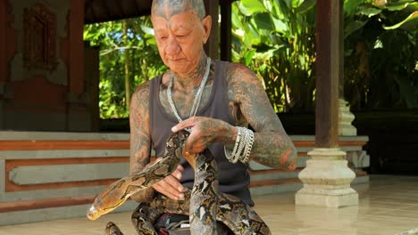 Slow-motion-parallax-shot-of-a-traditional-snake-tamer-in-a-balinese-temple-wearing-a-snake-around-his-neck-and-elegantly-controlling-it-in-bali-indonesia