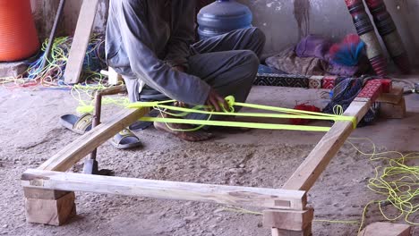 Worker-Weaving-Yellow-Thread-To-Make-Charpai-A-Traditional-Woven-Bed-In-Sindh,-Pakistan