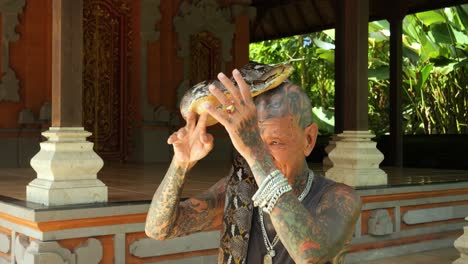 Slow-motion-shot-of-a-traditional-snake-charmer-in-a-balinese-temple-wearing-a-snake-around-his-neck-and-elegantly-controlling-it
