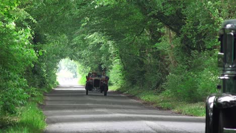 Vintage-cars-driving-down-a-long-narrow-country-road-in-Kildare-Ireland-on-a-balmy-Sunday-afternoon-in-summer
