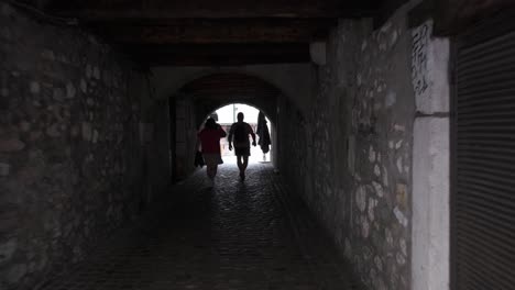 People-walking-through-dark-and-arched-passageway-near-riverbank-in-Annecy,-France