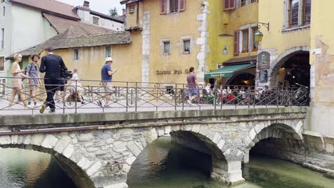 Tourists,-pedestrians-on-a-stone-bridge-in-Annecy-with-beautiful-architecture