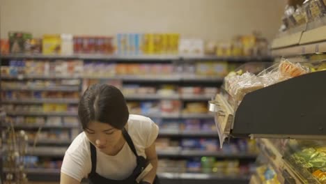 Asian-girl-worker-puts-goods-on-the-shelf.-Filling-shelves-with-goods.-Shop-work